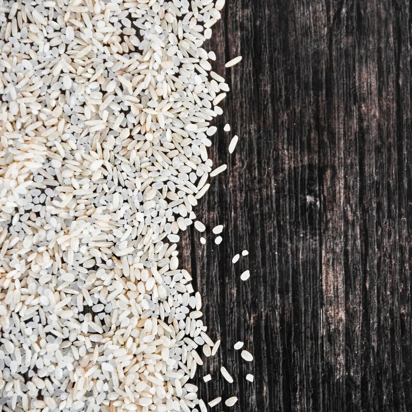 Uncooked white rice spread across a wooden background.