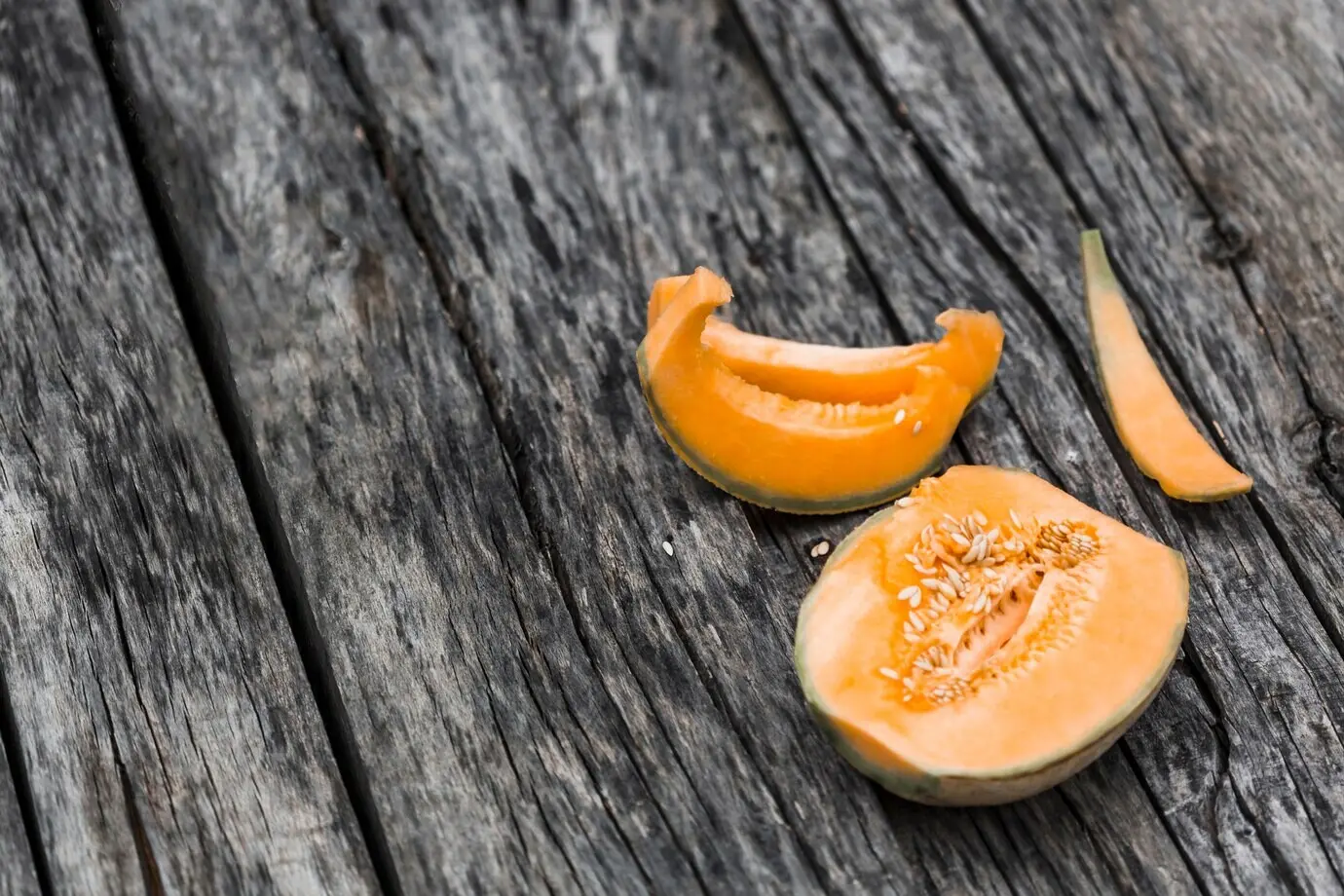 Halves and slices of musk melon on an old wooden table